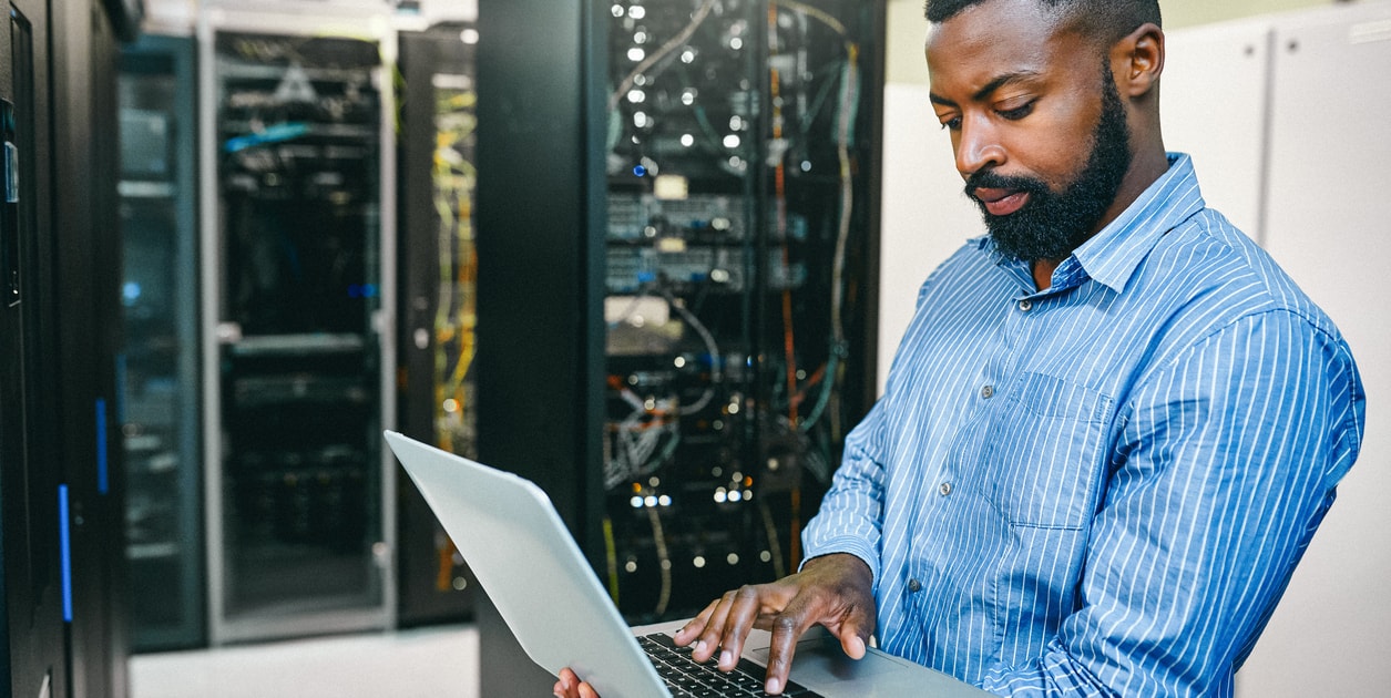 Shot of a young man using a laptop while working in a server room